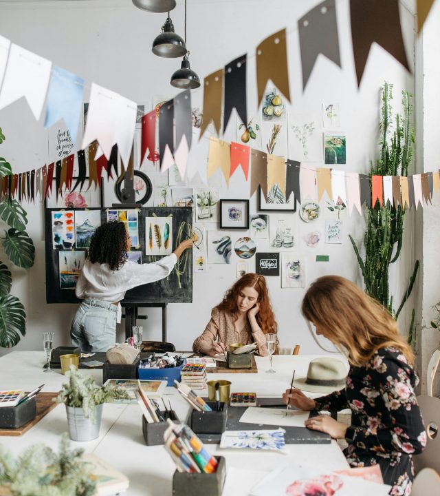 Artists paint in a bright, creative studio adorned with artwork and plants, fostering a vibrant atmosphere.
